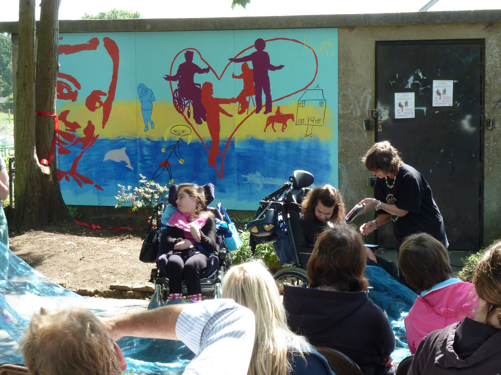 This photo shows two wheelchair users in front of the Happy section of the mural.